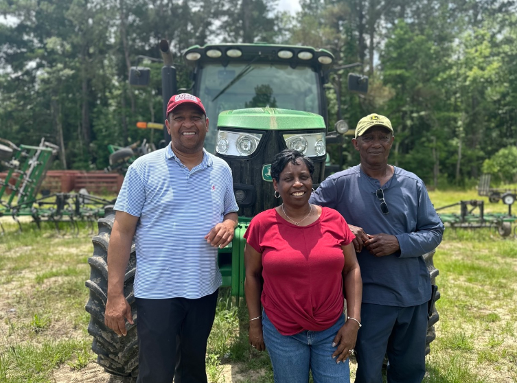 A picture of an African-American family standing and smiling in front of a green tractor on a farm.